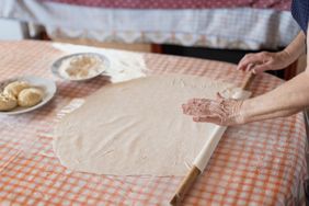 Woman skillfully rolls out dough on a checkered tablecloth in a cozy kitchen, preparing for a delightful cooking experienc