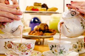 Proper Rose Garden's afternoon tea. Two people pouring tea into cup from teapots.