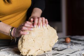 A person rolling dough on a counter of a home kitchen.