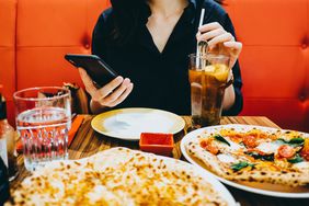 A woman on her phone while at a pizza restaurant. 