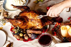 A person carving a turkey on a table with candles, cranberry sauce and mashed potatoes. 