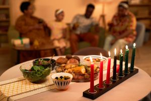 Colorful burning candles and tasty dishes on table in living room of family celebrating Kwanzaa