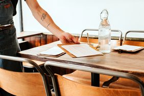 A server placing menus onto a table neat a bottle of water. 