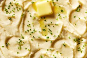 A close-up shot of mashed potatoes with chopped chives and a meting pat of butter. 