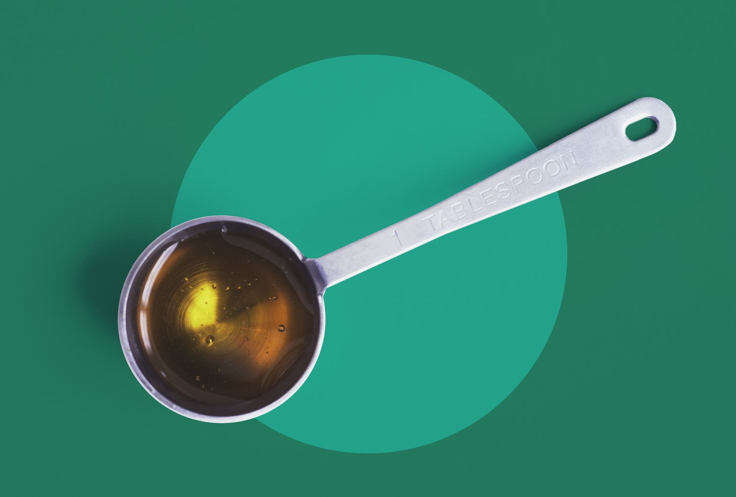 Honey in a measuring spoon on a green background. 