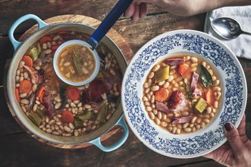 A white bean soup with pork being ladled into a bowl.