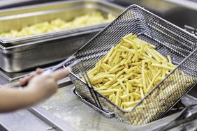 Female hands holding a frying pan with french fries at a commercial kitchen.