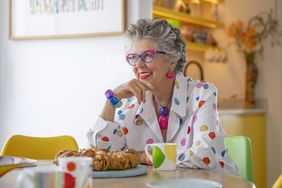 Prue Leith in a rainbow spotted shirt, sitting at a table. 