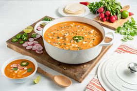 Le Creuset dutch oven filled with a fall soup on a cutting board surrounded by veggies