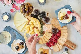 A party tray covered with cheese, fruit and crackers on a table with place settings and wine