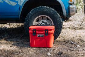 The Yeti Roadie 15 Hard Cooler sitting on the ground in front of the tire of a car