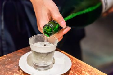 Sake being poured into a cup from a green bottle. 