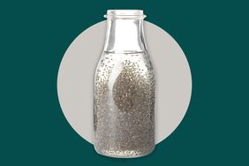 A glass bottle with water and chia seeds in front of a grey and teal background.