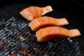 Salmon being grilled over charcoal.