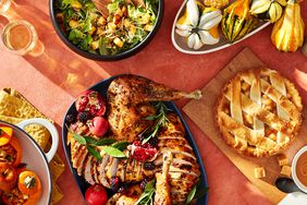 A Thanksgiving table with carved turkey, salad, pie, gourds, stuffed pumpkin and drinks. 