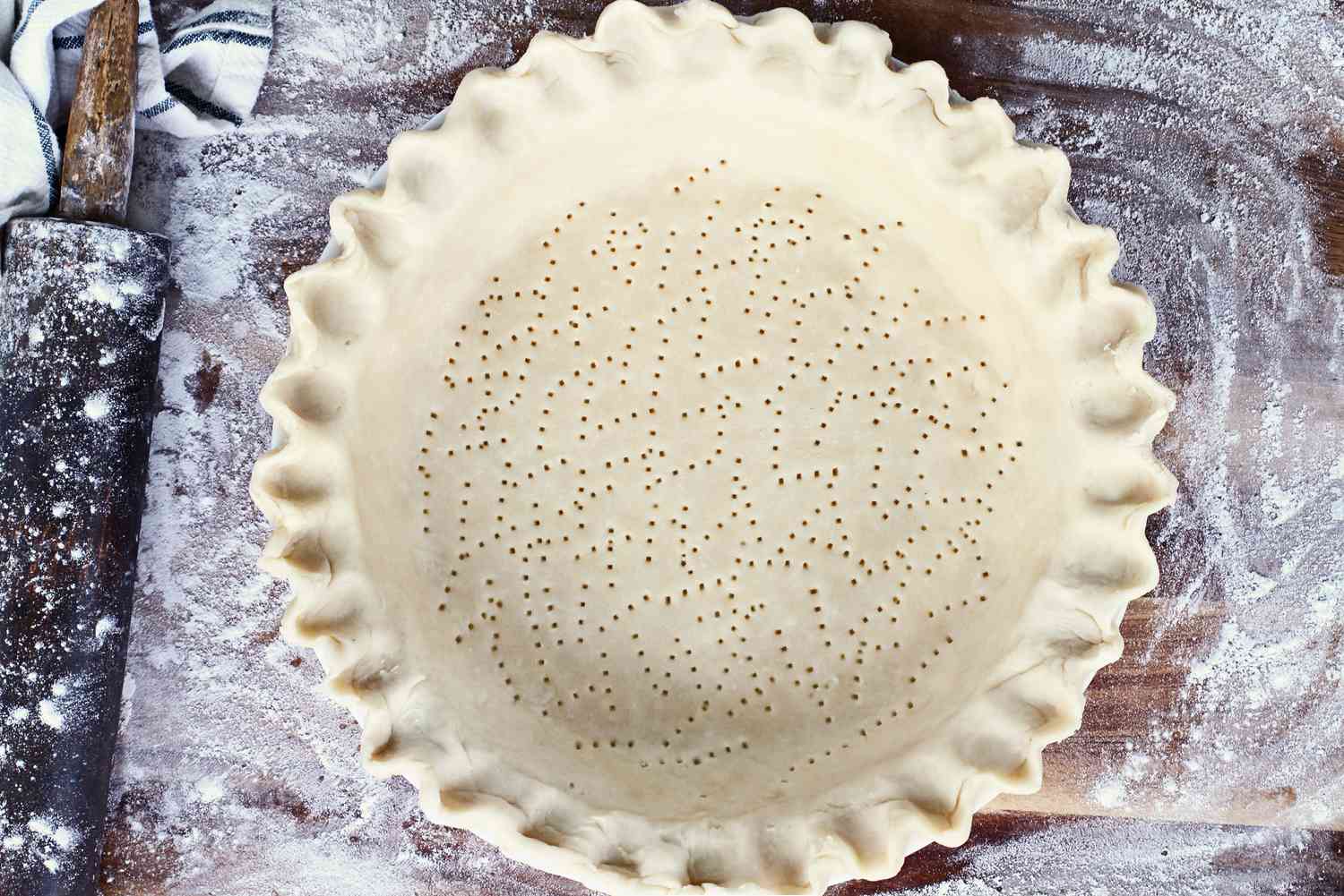 A pie crust with a fluted edge that has been perforated with fork, next to a rolling pin.