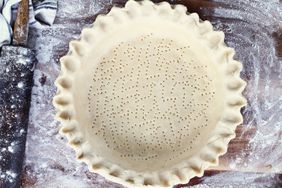 A pie crust with a fluted edge that has been perforated with fork, next to a rolling pin.