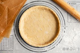 Raw pie crust in a fluted pan on a floured work surface with a French rolling pin and unbleached parchment paper