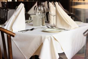 A restaurant dinner table under natural light has been set with linens, silverware and stemware, and awaits its dinner clientele.