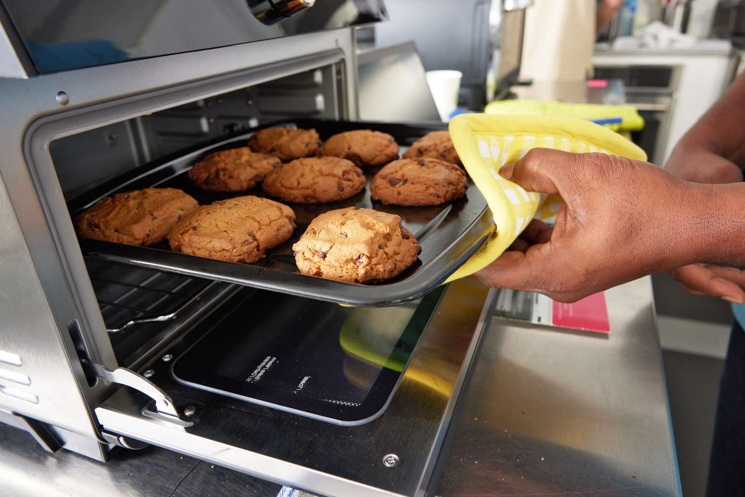 Hand using a potholder to pull a sheet of baked cookies from the Instant Pot Omni Plus Air Fryer Toaster Oven