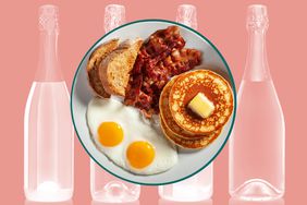 A plate with two eggs, toast, bacon and buttered pancakes over a background of sparkling wine bottles. 