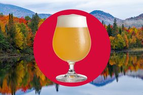 Fall foliage reflecting in a lake behind a glass of cold cider. 