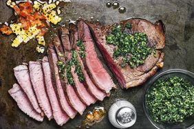 Sliced steak with corn and pepper relish and pesto sauce on a metal background.