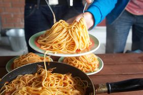 Giant servings of spaghetti being served on plates.